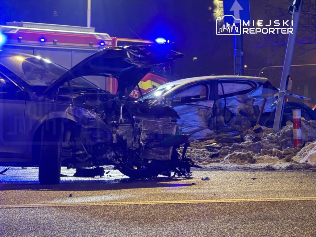 Dwa uszkodzone samochody osobowe po wypadku drogowym, otoczone przez policyjne i strażackie pojazdy.
