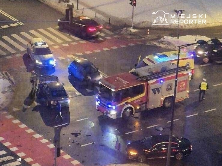 Na skrzyżowaniu z widocznymi pojazdami ratunkowymi oraz osobowymi doszło do stłuczki. W tle widać policjanta kierującego ruchem.