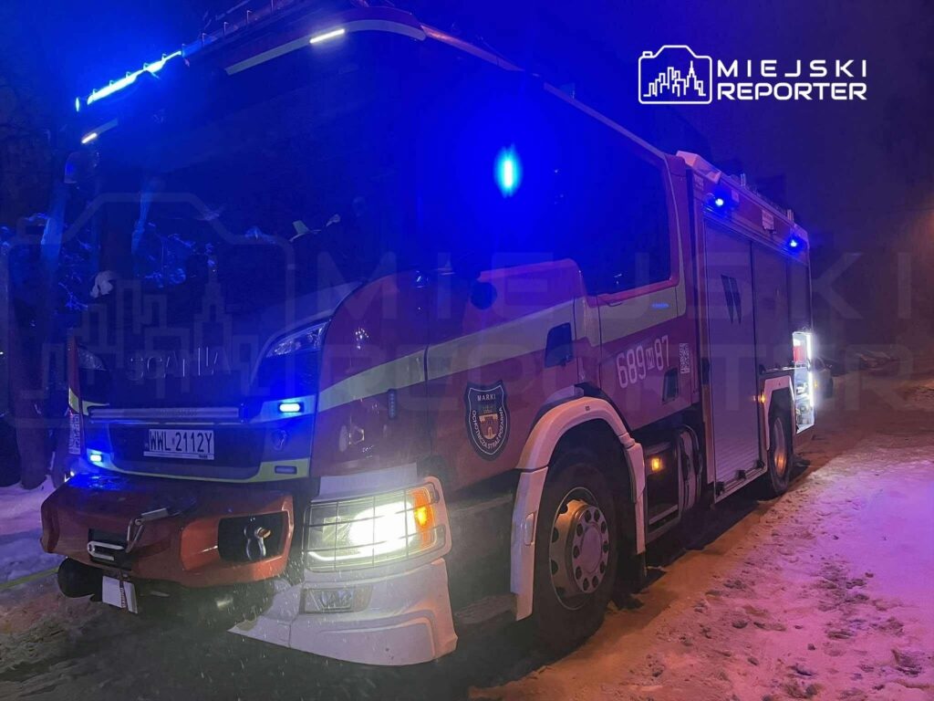 Czerwony wóz strażacki z niebieskimi światłami stoi na zaśnieżonej ulicy w nocy.
