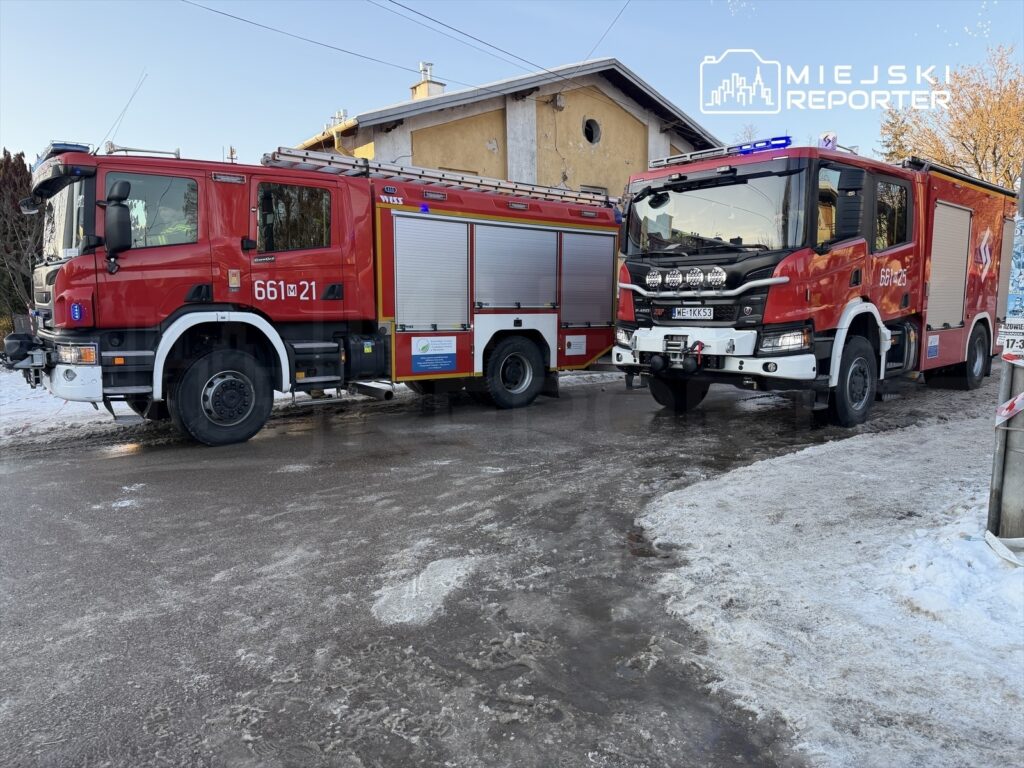 Dwa wozy strażackie zaparkowane na zaśnieżonej ulicy obok budynku mieszkalnego.
