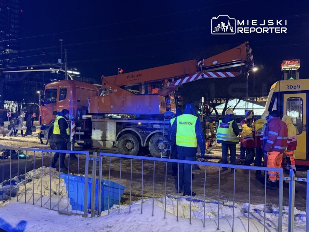 Ekipa ratunkowa pracuje przy unieruchomionym tramwaju, obok znajduje się ciężarówka z podnośnikiem.