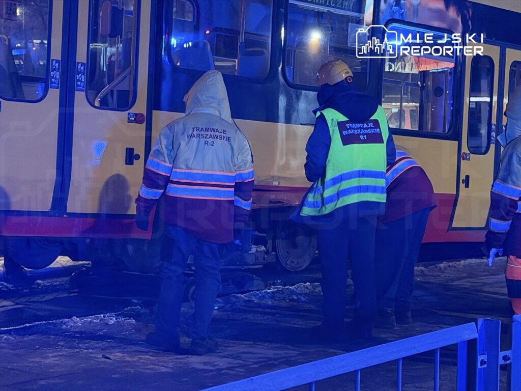 Grupa pracowników w odblaskowych kamizelkach pracuje przy tramwaju na oświetlonym torowisku w nocy.