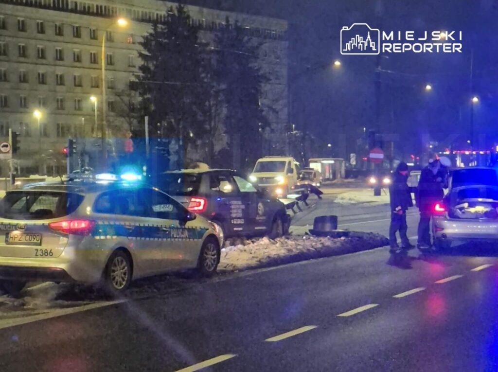 Policjanci w mundurach sprawdzają dokumenty kierowcy w pobliżu zaparkowanego radiowozu na ośnieżonej ulicy.