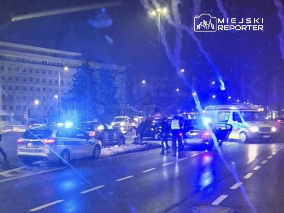 Grupa funkcjonariuszy policji prowadzi interwencję na drodze, otoczeni przez zaparkowane radiowozy i karetkę.