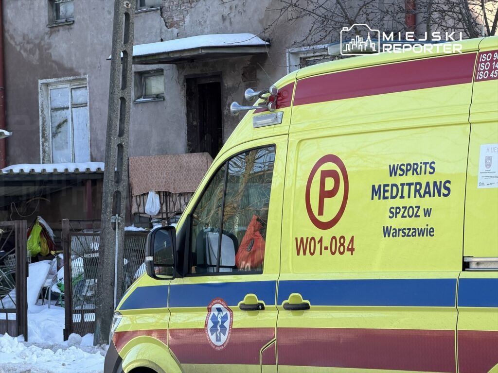 Karetka pogotowia z napisem "WSPRITS MEDITRANS SPZOZ w Warszawie" zaparkowana obok budynku w zimowym otoczeniu.