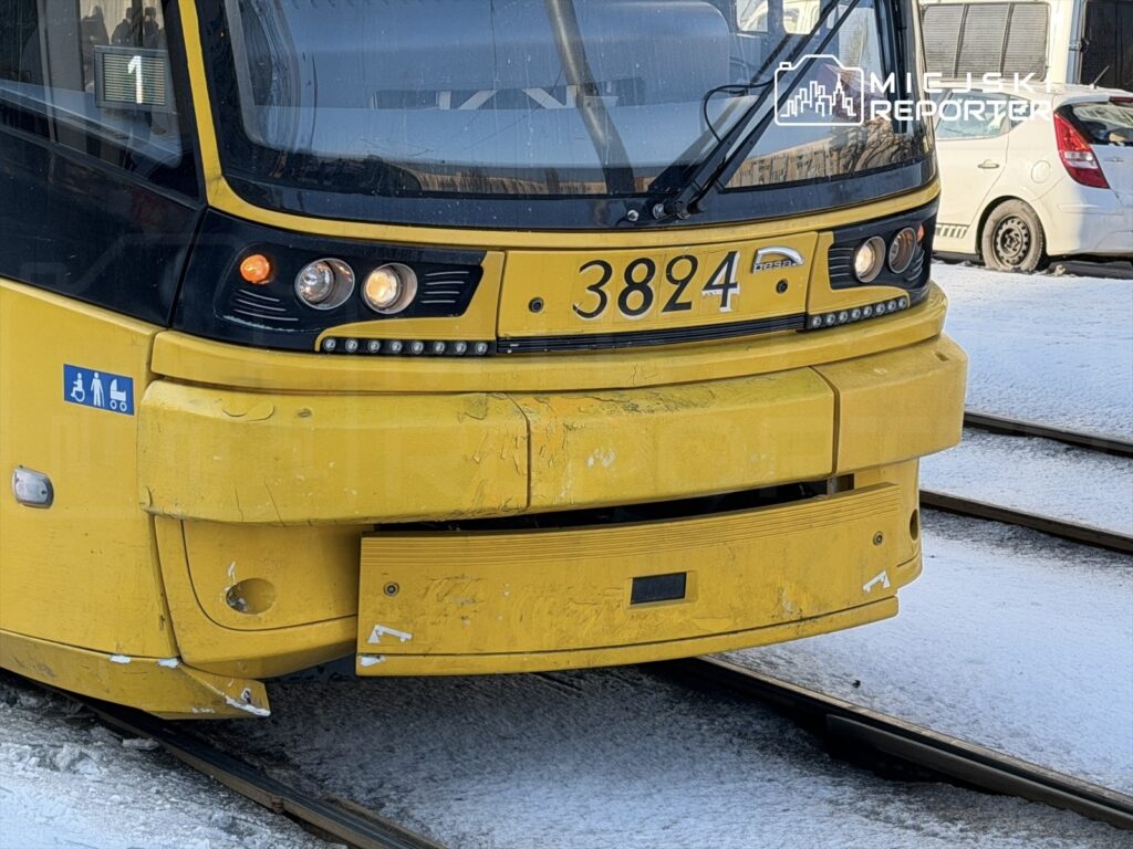 Żółty tramwaj z numerem 3824 stojący na torach w zimowej scenerii, z widocznym śniegiem na ziemi.