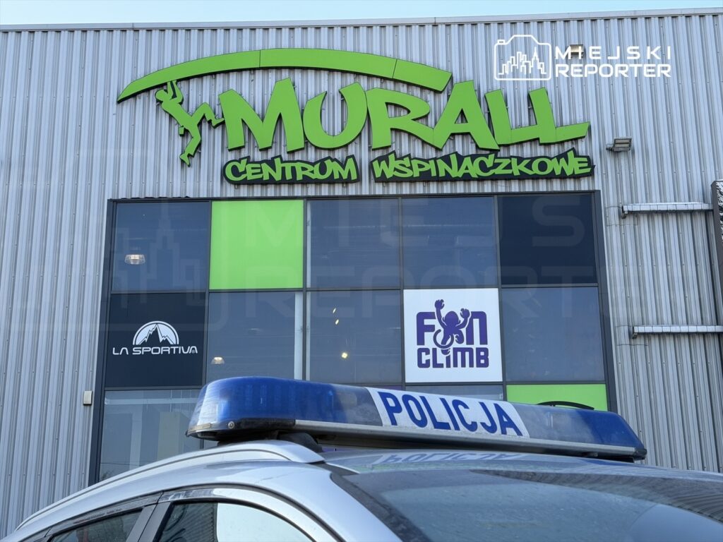 W samochodzie policyjnym z niebieską sygnalizacją, zaparkowanym przed centrum wspinaczkowym Murall, widoczny jest jego znak.