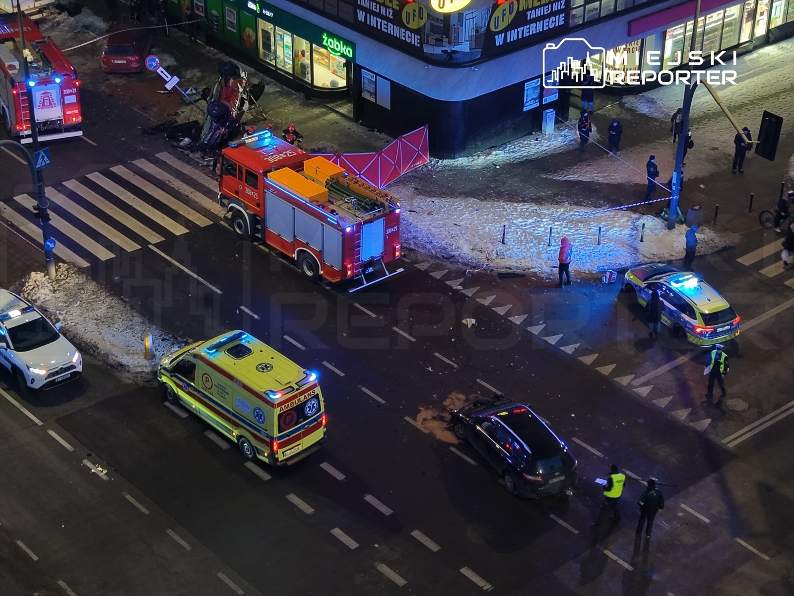 Zespół ratownictwa medycznego oraz straż pożarna interweniują przy przewróconym samochodzie na ruchliwej ulicy.