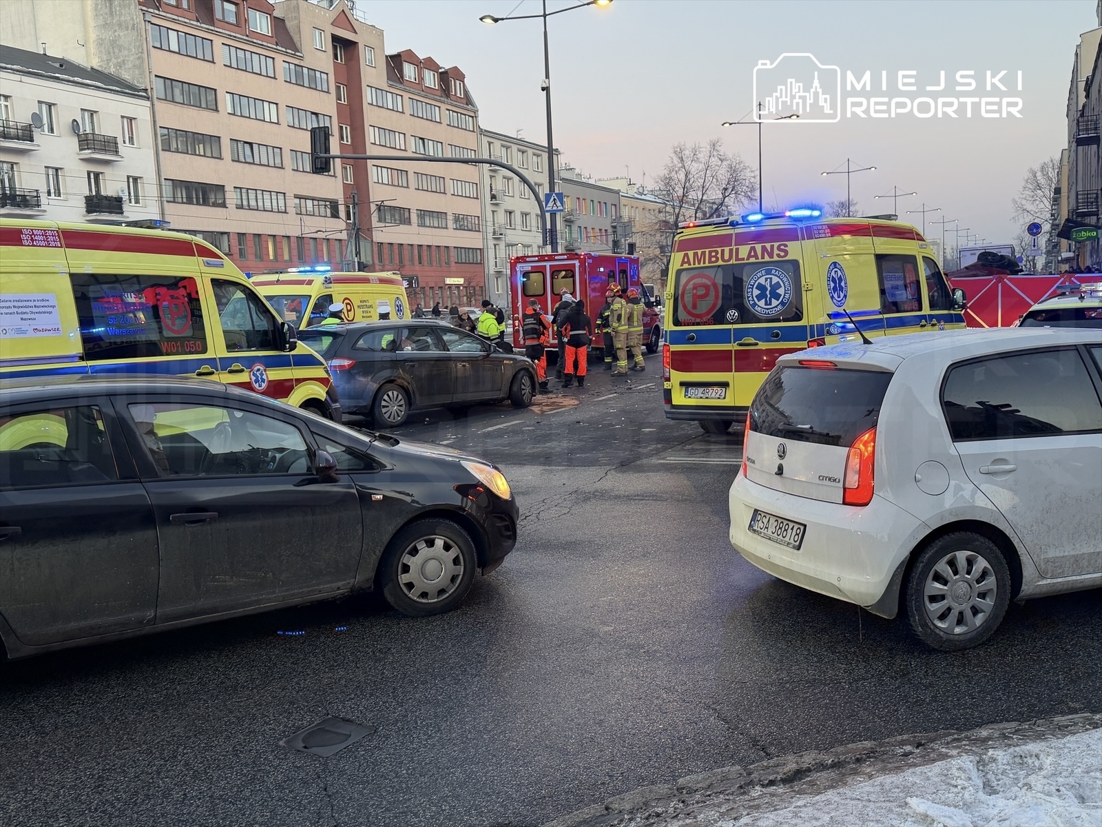 Ambulanse i strażacy pracują na miejscu wypadku drogowego w mieście, otoczeni przez zablokowane pojazdy.