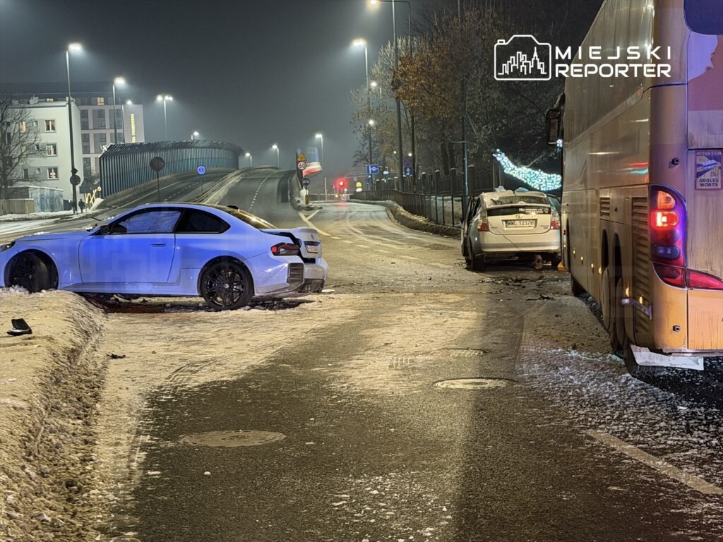 Dwa uszkodzone samochody na ośnieżonej drodze, jeden z nich stoi na poboczu, a obok kursuje autobus.