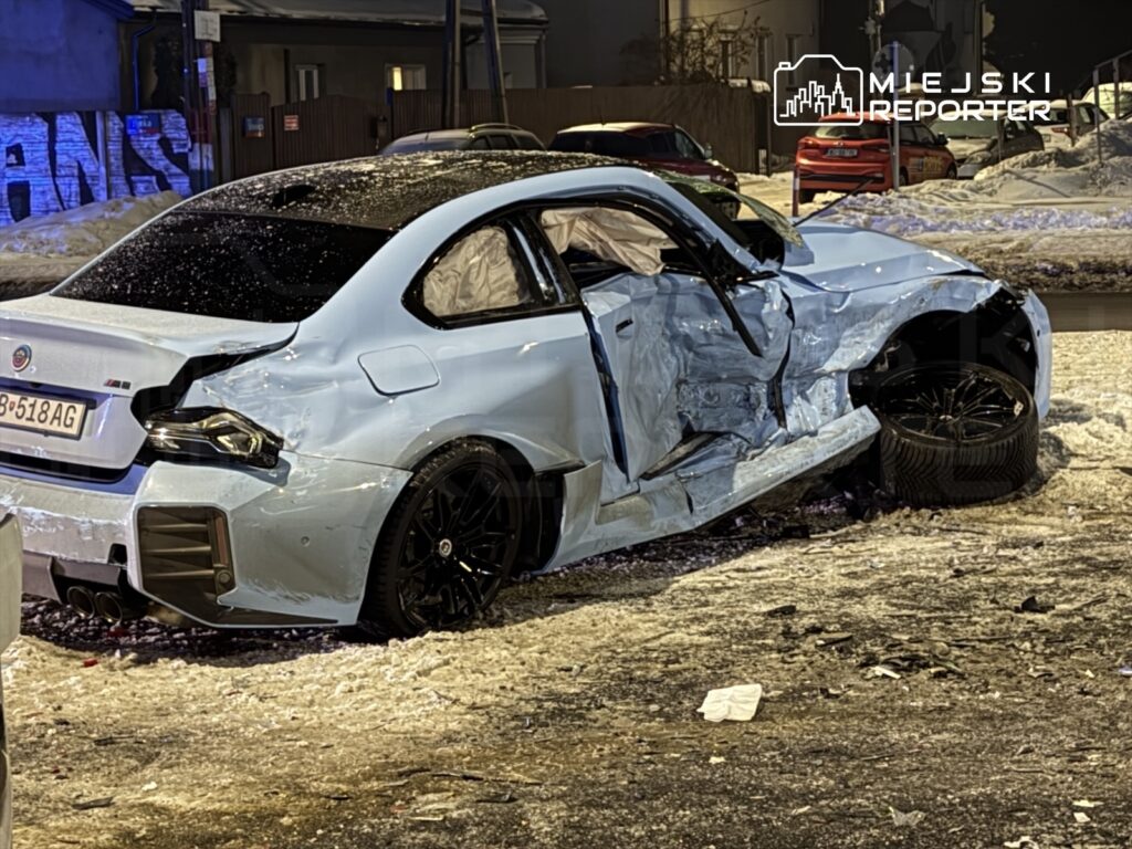 Uszkodzony niebieski samochód osobowy z otwartymi drzwiami stoi na ośnieżonej ulicy w nocy.