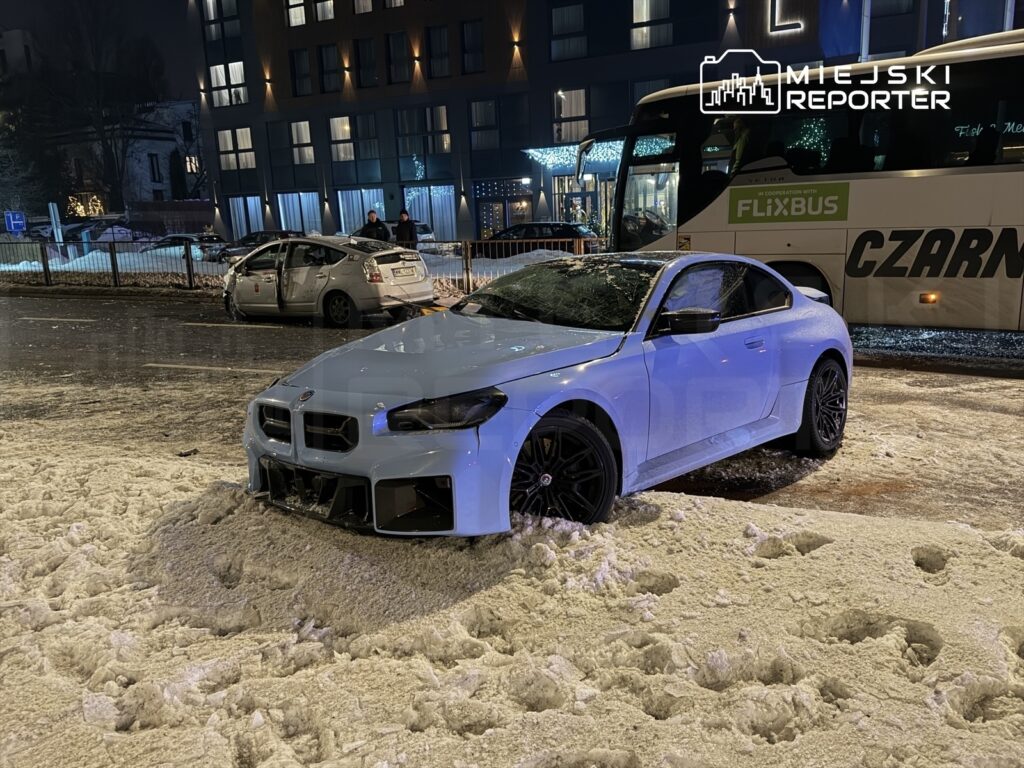 Biały samochód sportowy utknął w śniegu na zaśnieżonej ulicy, obok uszkodzony pojazd i autobus FlixBus.