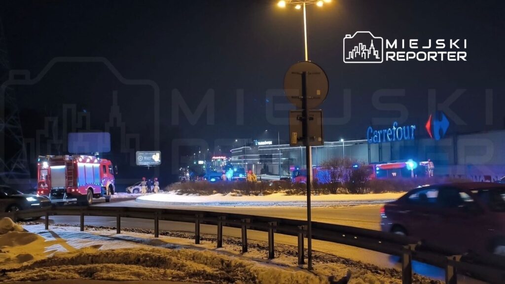 W nocy przy supermarkecie Carrefour zjeżdżają samochody strażackie, a służby interwencyjne pracują na miejscu zdarzenia.