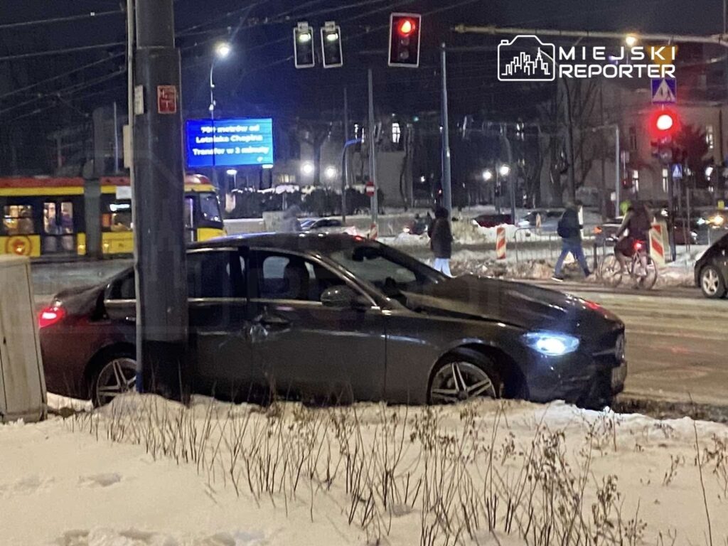 Czarny samochód osobowy stoi na poboczu w śnieżnym otoczeniu, obok przejścia dla pieszych i tramwaju.