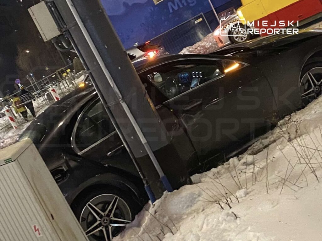 Czarny samochód osobowy zaparkowany na zaśnieżonej ulicy, obok widać oznakowanie drogowe.