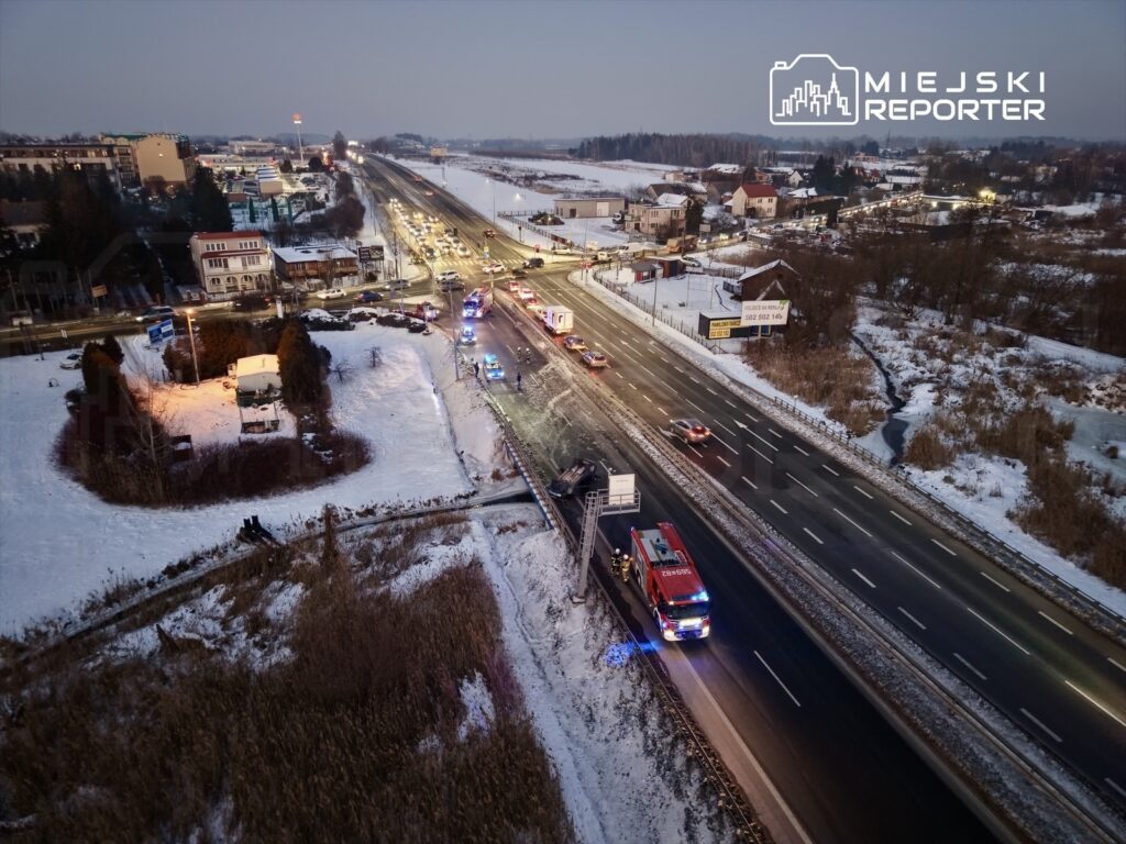 Na drodze w zimowym otoczeniu widać pojazdy ratunkowe oraz policyjne, które interweniują przy wypadku.