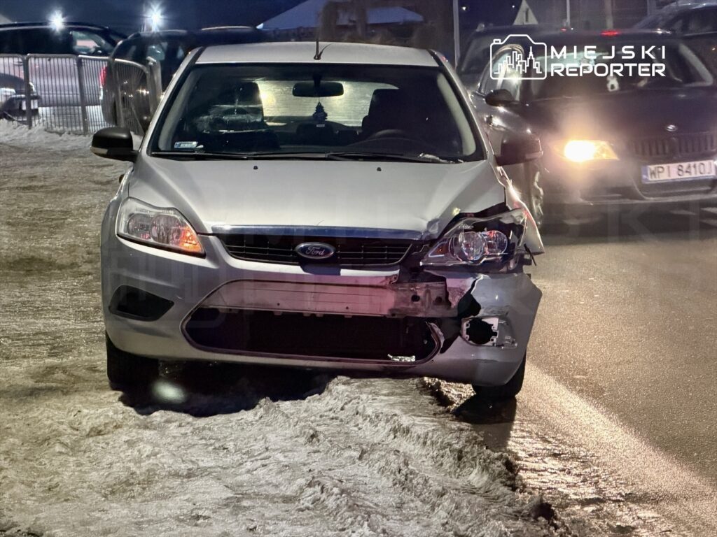 Uszkodzony samochód osobowy marki Ford zaparkowany na poboczu drogi, z widocznymi uszkodzeniami przodu.