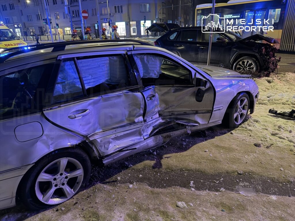 Uszkodzony samochód osobowy z wgniecioną stroną stoi na oświetlonej ulicy, obok widać pojazd z uszkodzeniami tyłu.