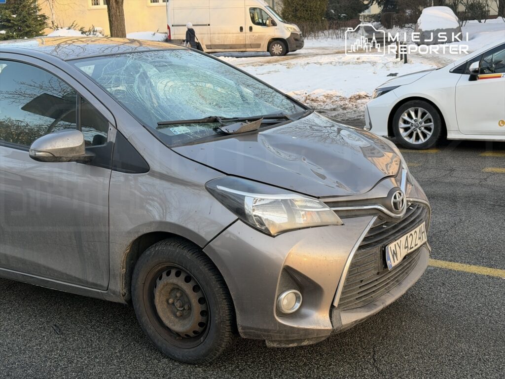 Uszkodzony samochód osobowy z rozbitą szybą przednią zaparkowany na ulicy w otoczeniu śniegu.