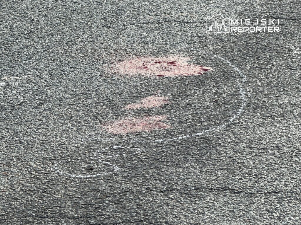 Czerwony ślad na asfalcie w kształcie pytajnika otoczony białą linią.