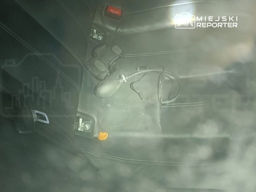 Czarna skóra tylnej kanapy samochodu z widocznym zestawem narzędzi i przewodem.