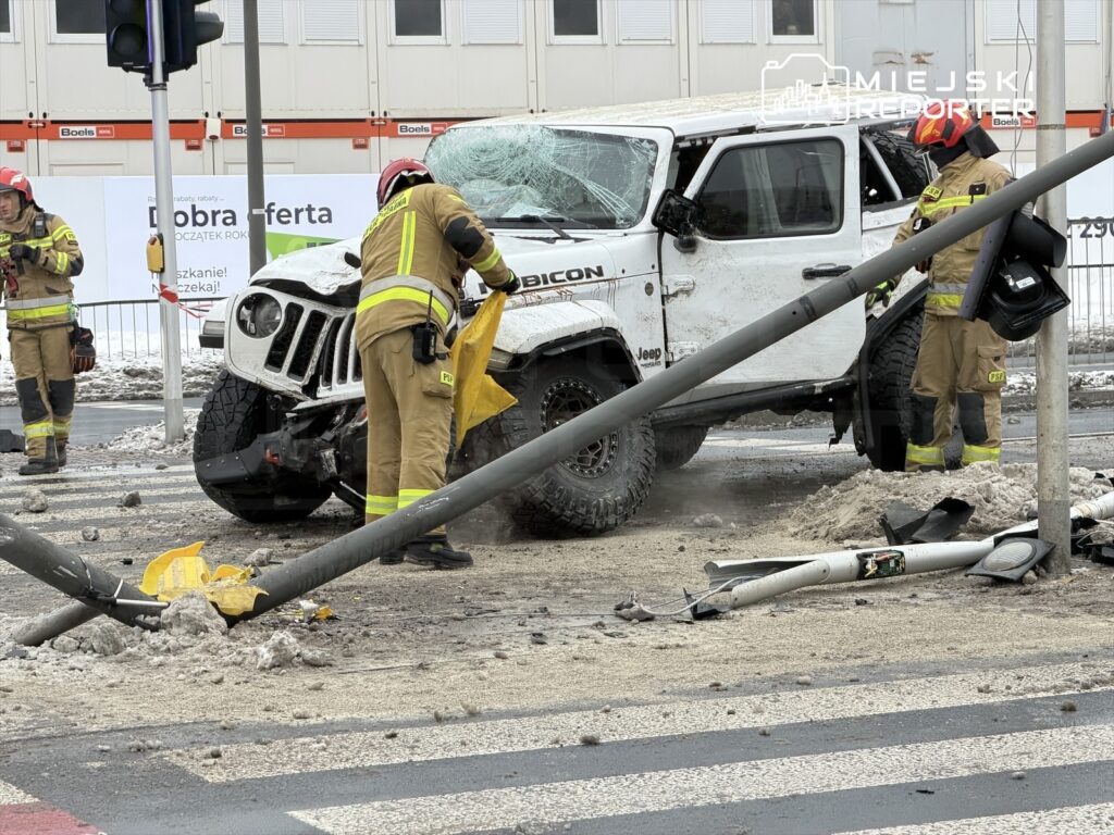 Strażacy usuwają uszkodzenia po wypadku samochodowym, w którym jeep uderzył w latarnię na zamarzniętej ulicy.