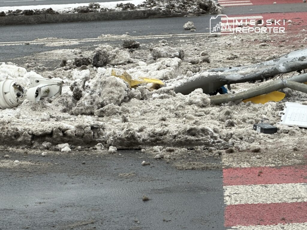 Złamany słup oświetleniowy leży na zaśnieżonej jezdni, obok leżą resztki sprzętu i śniegu.