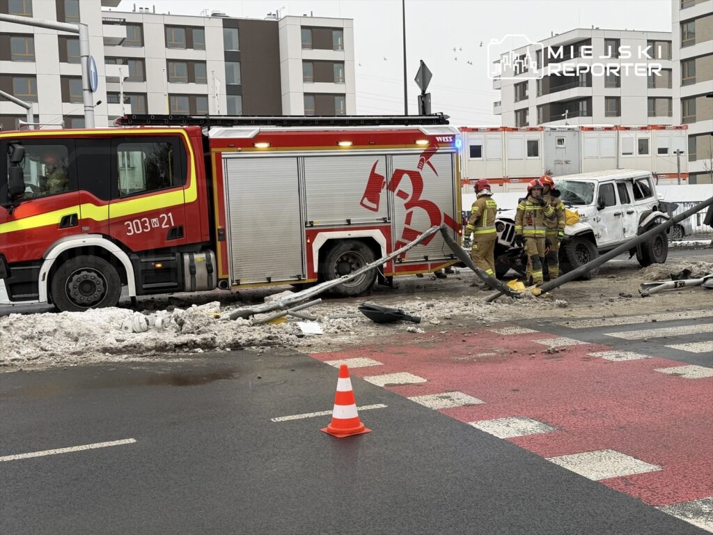 Strażacy w mundurach pracują przy uszkodzonym pojeździe w pobliżu wozu strażackiego na zaśnieżonej jezdni.