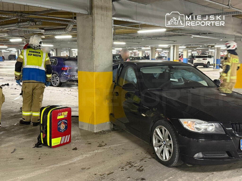 Strażacy w mundurach, jeden z nich z plecakiem medycznym, interweniują w podziemnym parkingu po incydencie z samochodami.