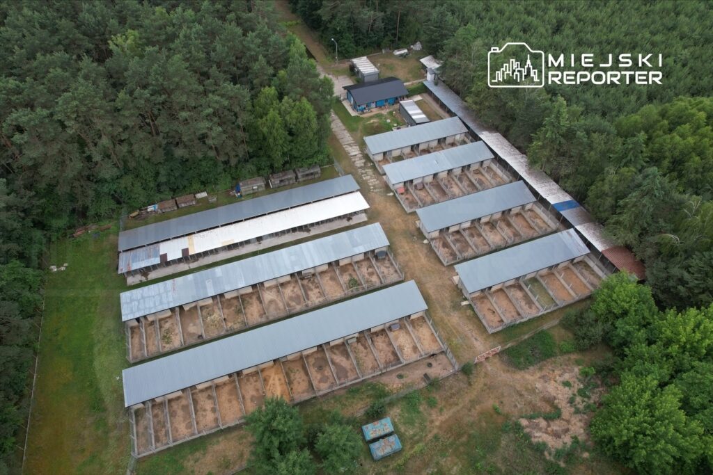 Widok z lotu ptaka na zagrody w otoczeniu lasu, z metalowymi zadaszeniami i wyraźnie wytyczonymi alejkami.