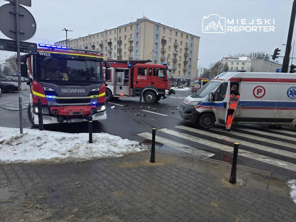 Zespół ratunkowy przy ambulansie sprawdza sytuację po wypadku drogowym na skrzyżowaniu, obok pojazdów straży pożarnej.
