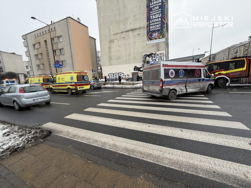Na skrzyżowaniu zatrzymane karetki pogotowia i straż pożarna, obok przejścia dla pieszych. W tle widoczny mural na ścianie budynku.