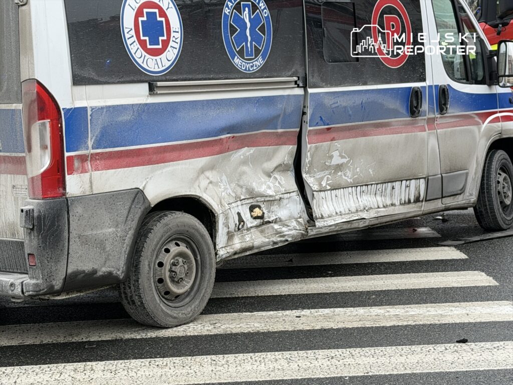 Karetka pogotowia z uszkodzeniem bocznym stoi na przejściu dla pieszych na miejskiej ulicy.