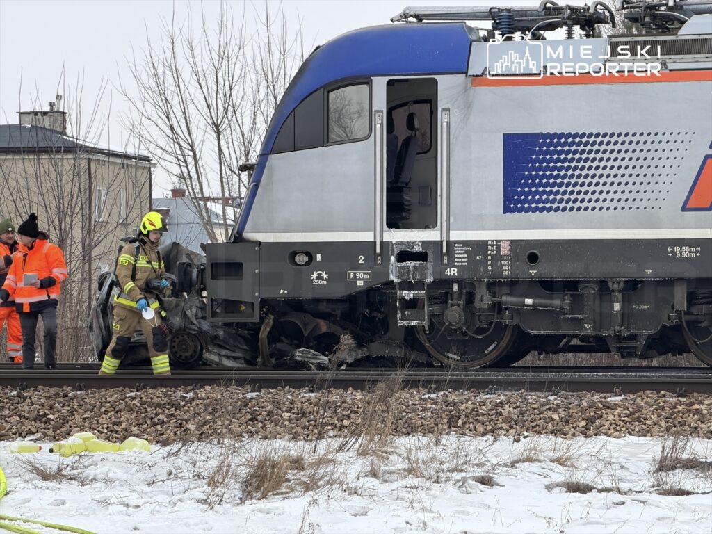 Strażacy w specjalistycznym sprzęcie pracują przy uszkodzonej lokomotywie na torach, w zimowym otoczeniu.