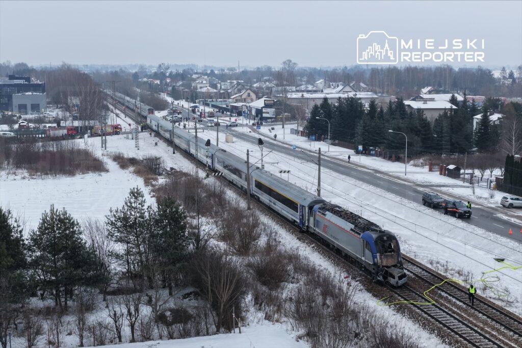 Pociąg towarowy wykolejony na stacji kolejowej, w otoczeniu śniegu i drzew, z obecnością służb ratunkowych.