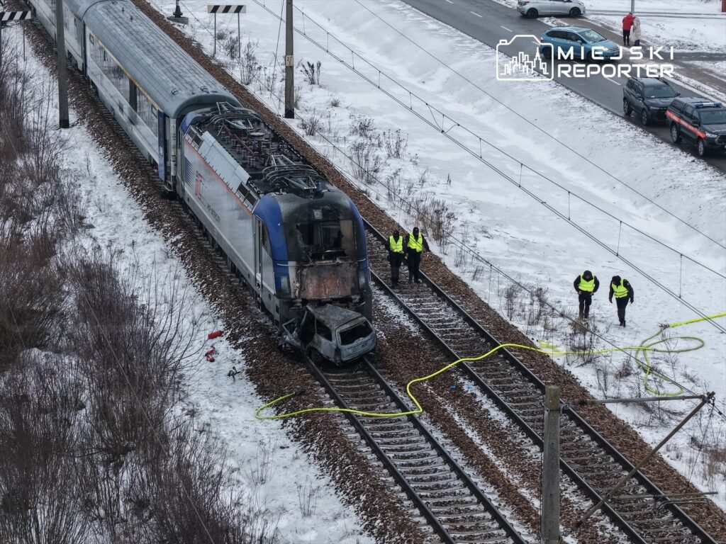 Zespół ratunkowy w kamizelkach odblaskowych bada uszkodzony pociąg na zaśnieżonej linii kolejowej.