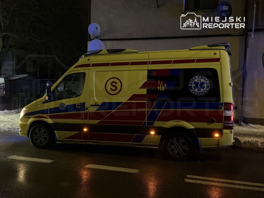 Zespół ratownictwa medycznego w żółtej karetce stoi na oświetlonej ulicy w nocy.