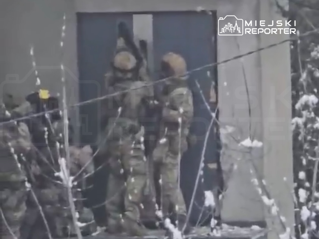 Grupa żołnierzy w kamuflażu otwiera drzwi budynku w zaśnieżonym otoczeniu.