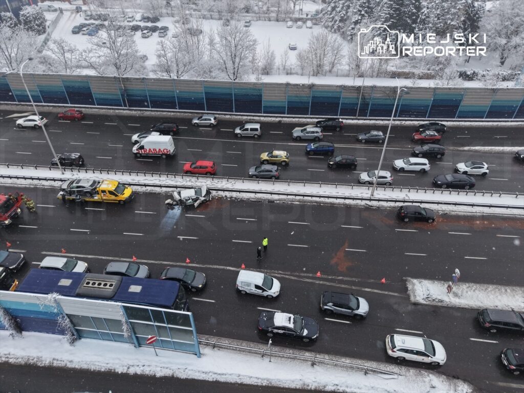 Wielopojazdowy wypadek na drodze, w tle śnieżne otoczenie, a w pobliżu pracują służby ratunkowe.