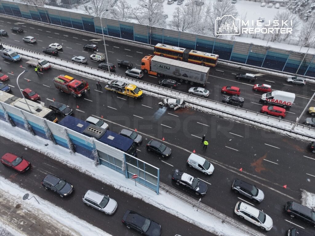 Zablokowany ruch na drodze, w tle widoczne pojazdy służb ratunkowych oraz oznakowanie ostrzegawcze.