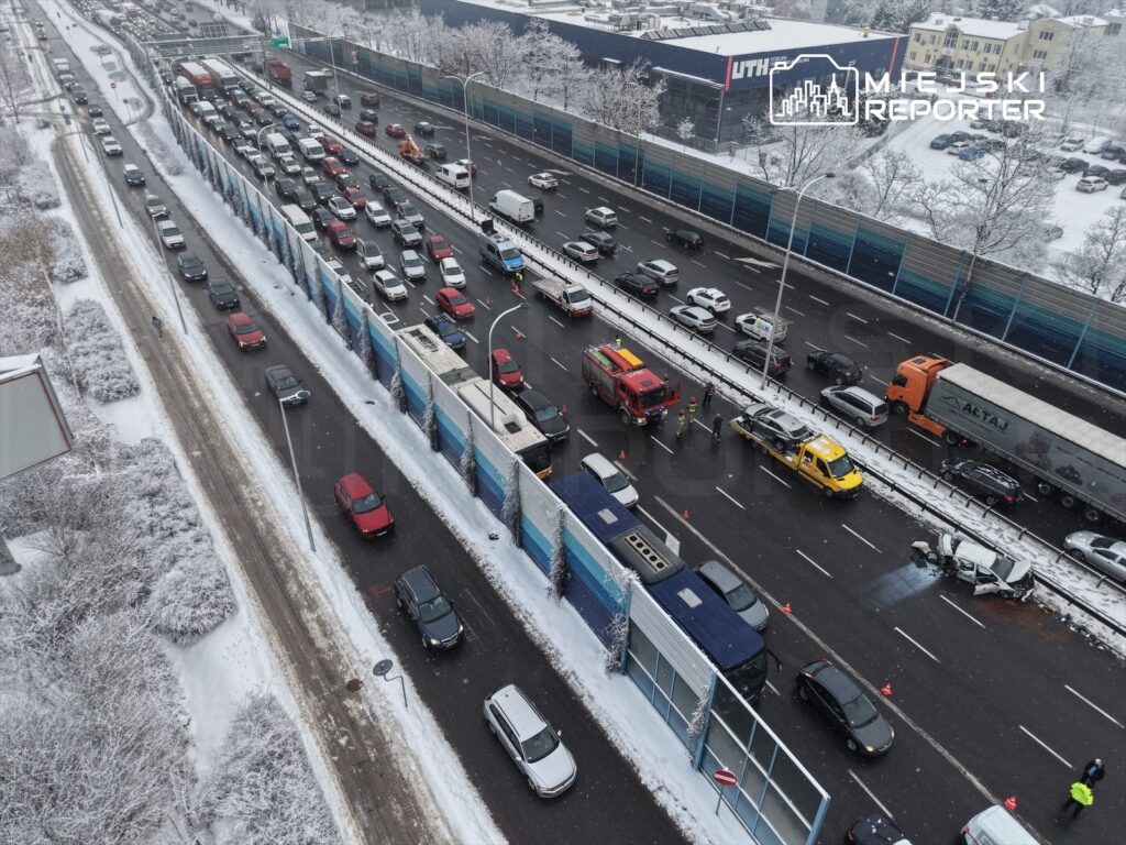 Zator drogowy na trasie z powodu wypadku, w którym uczestniczyły dwa pojazdy; w tle śnieg i budynki.