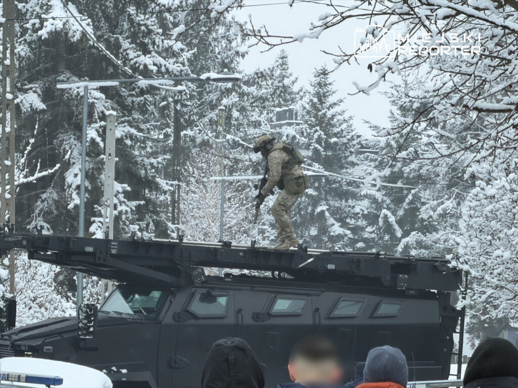 Żołnierz w kamuflażu wykonujący ćwiczenia na dachu opancerzonego pojazdu w zimowym otoczeniu z zaśnieżonymi drzewami.