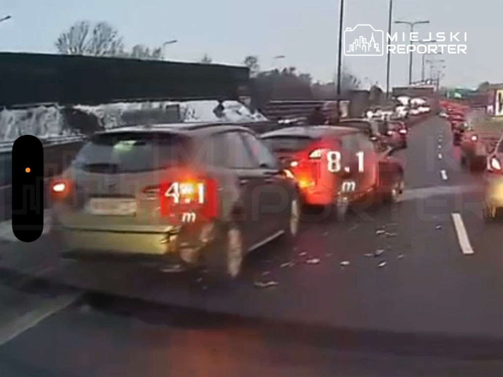 Ruch samochodowy w korku na drodze, z widocznymi pojazdami osobowymi i oznaczeniami odległości.