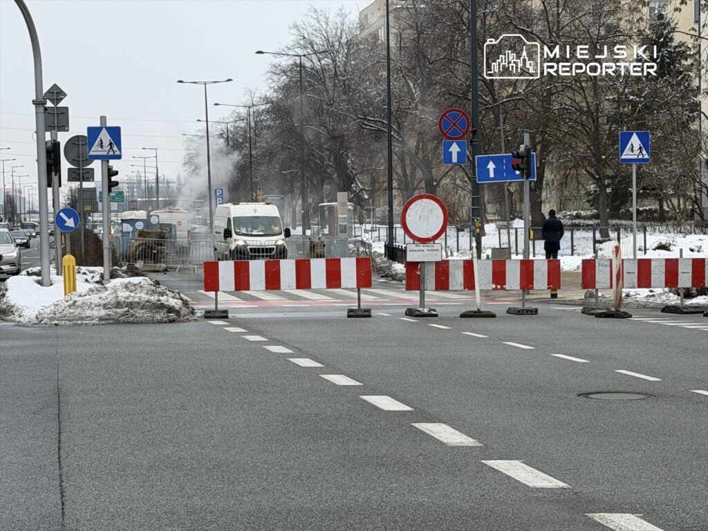 Przejazd zamknięty z powodu prac drogowych, w tle widoczny samochód dostawczy i barierki ochronne.