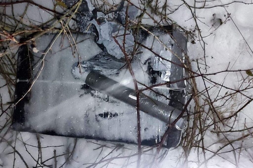 Zniszczony telewizor leży na śniegu, otoczony gałęziami i resztkami materiałów.