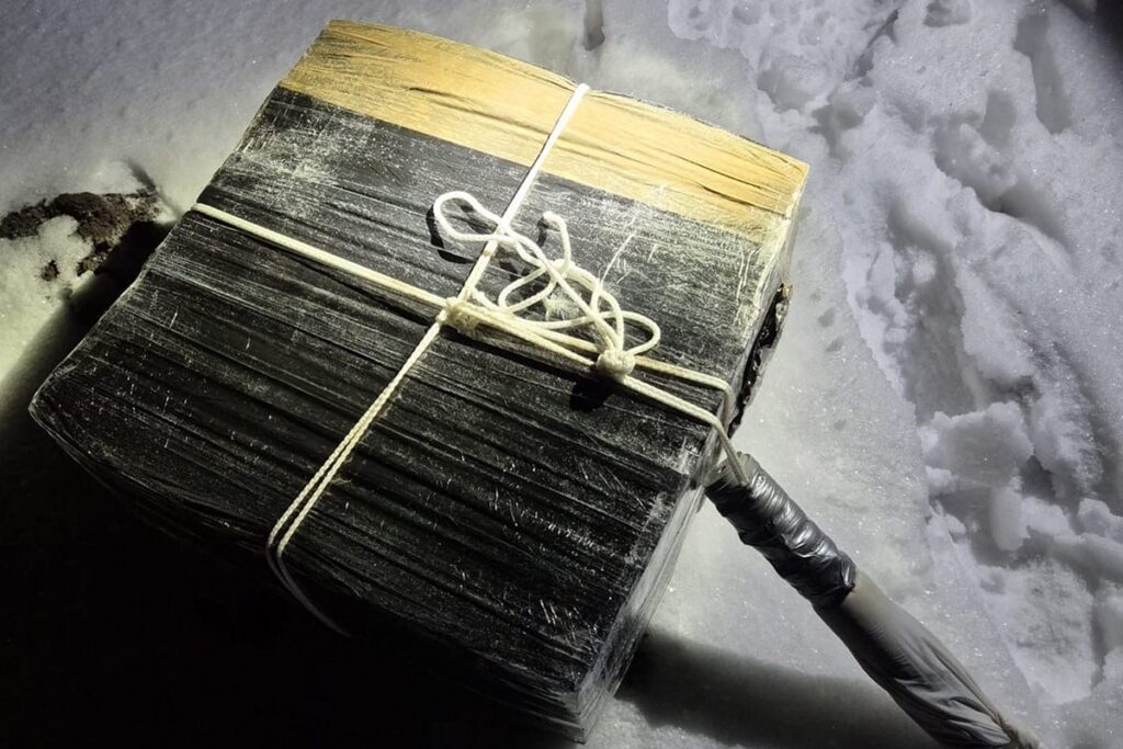 Pakunek owinięty w folię, związany sznurkiem, leży na śniegu w ciemnym otoczeniu.