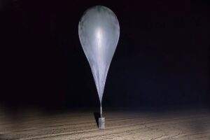 Balon meteorologiczny unosi się nad pustynnym terenem, połączony z urządzeniem na ziemi.