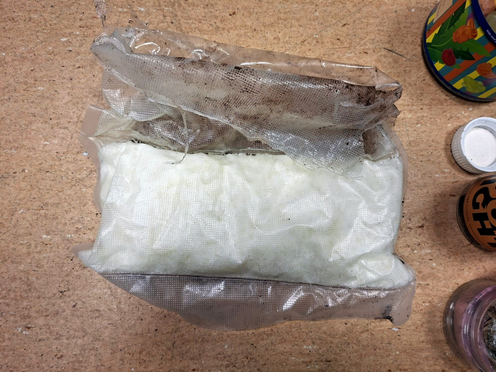 Pakunek z białym proszkiem umieszczony na drewnianym blacie, obok kilka pojemników i słoików.