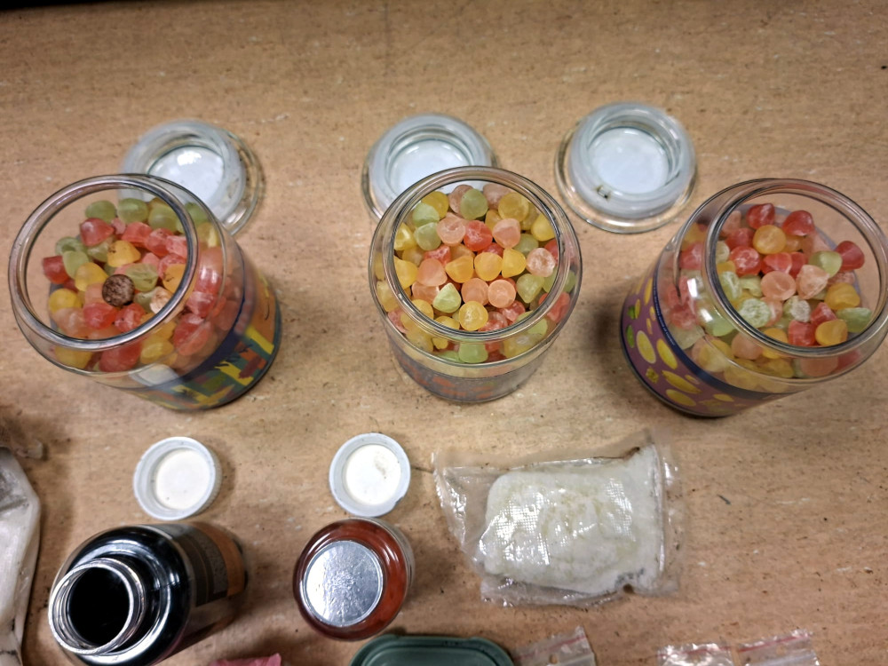 Trzy słoiki z kolorowymi żelkami na drewnianym blacie, obok leżą różne zakrętki i opakowania.