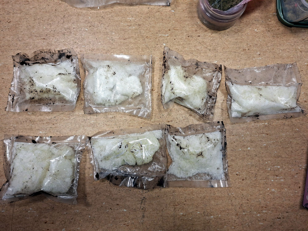 Siedem przezroczystych torebek z białym proszkiem ułożonych na drewnianym stole.